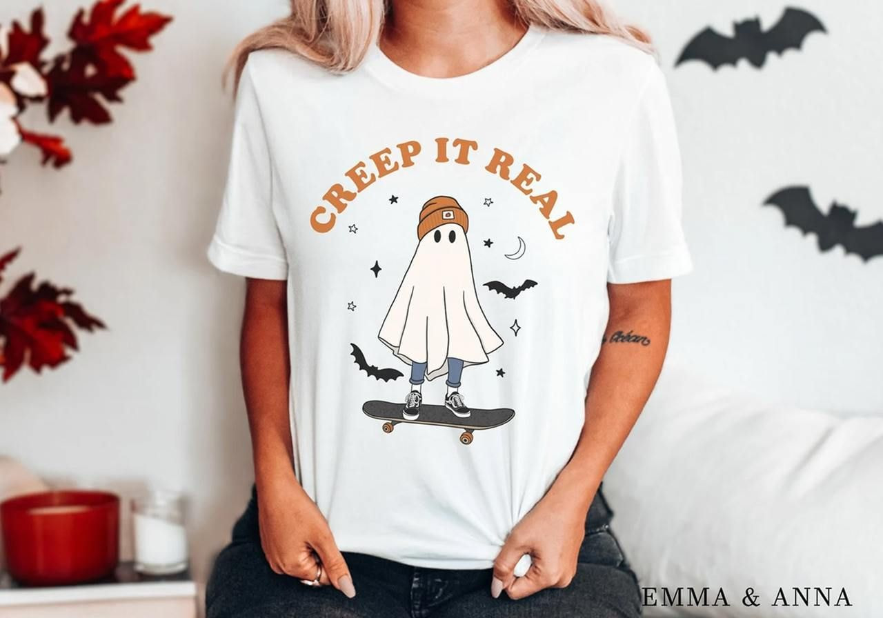 A woman in a white t-shirt with a cartoon ghost on a skateboard and "Creep It Real" text.